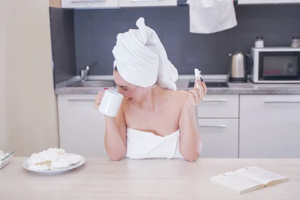 Молодая девушка сидит на кухне после душа завернутый в белое полотенце и отдыха — стоковое фото