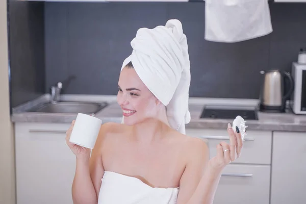 Young girl sitting in the kitchen after a shower wrapped in a white towel and resting — Stockfoto