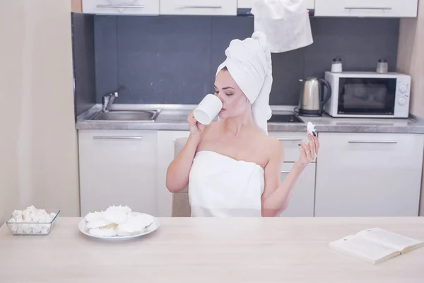 Joven sentada en la cocina después de una ducha envuelta en una toalla blanca y descansando — Foto de Stock