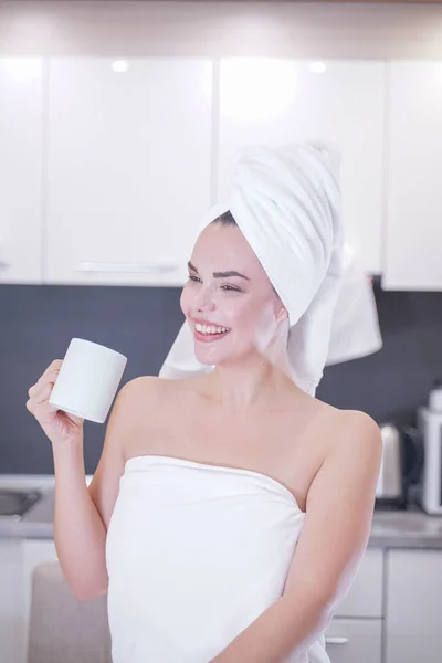 Giovane ragazza seduta in cucina dopo una doccia avvolta in un asciugamano bianco e riposante — Foto Stock