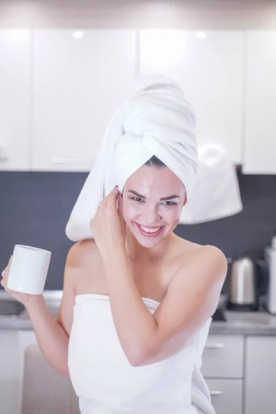 Young girl sitting in the kitchen after a shower wrapped in a white towel and resting — Stockfoto