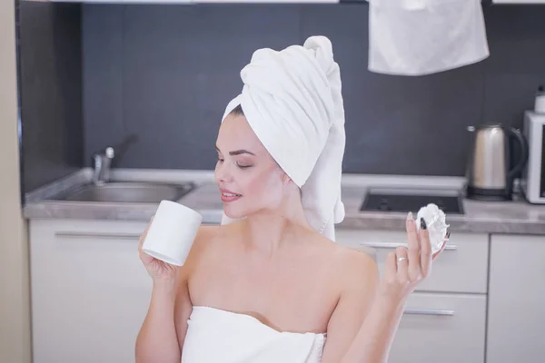 Young girl sitting in the kitchen after a shower wrapped in a white towel and resting — Stockfoto