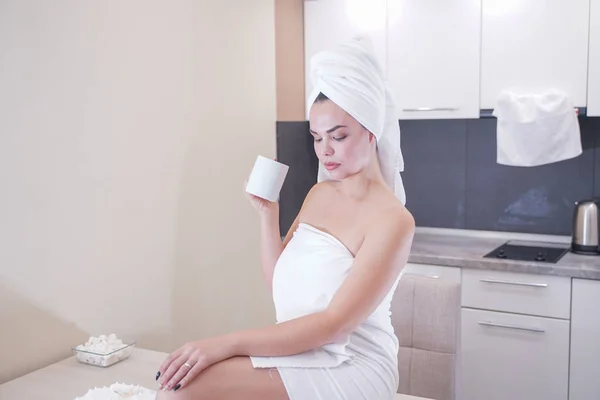 Joven sentada en la cocina después de una ducha envuelta en una toalla blanca y descansando — Foto de Stock