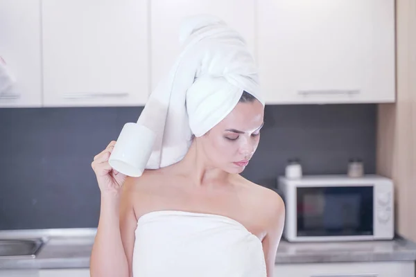 Joven sentada en la cocina después de una ducha envuelta en una toalla blanca y descansando — Foto de Stock