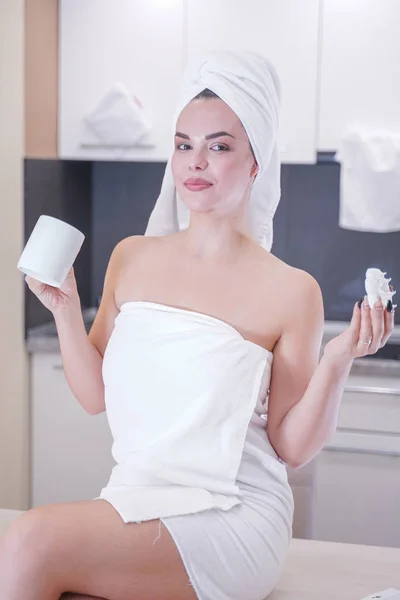 Young girl sitting in the kitchen after a shower wrapped in a white towel and resting — Stockfoto