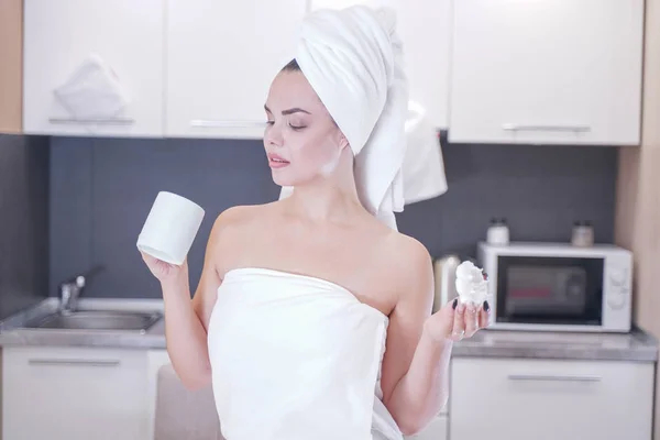 Young girl sitting in the kitchen after a shower wrapped in a white towel and resting — Stockfoto