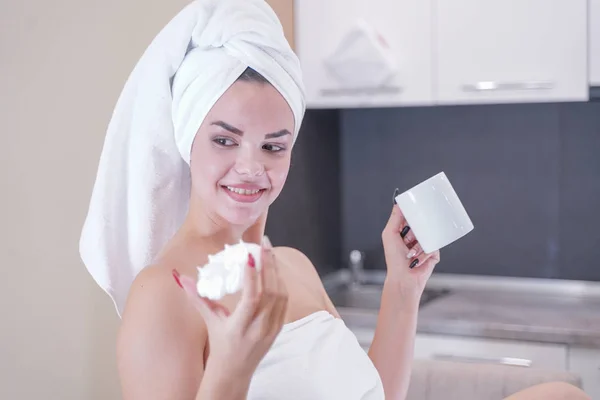 Young girl sitting in the kitchen after a shower wrapped in a white towel and resting — Stockfoto