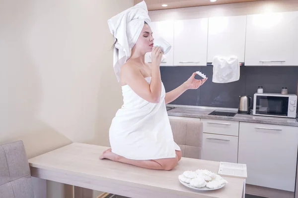 Молодая девушка сидит на кухне после душа завернутый в белое полотенце и отдыха — стоковое фото