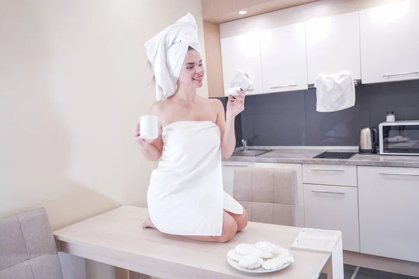Jeune fille assise dans la cuisine après une douche enveloppée dans une serviette blanche et se reposant — Photo