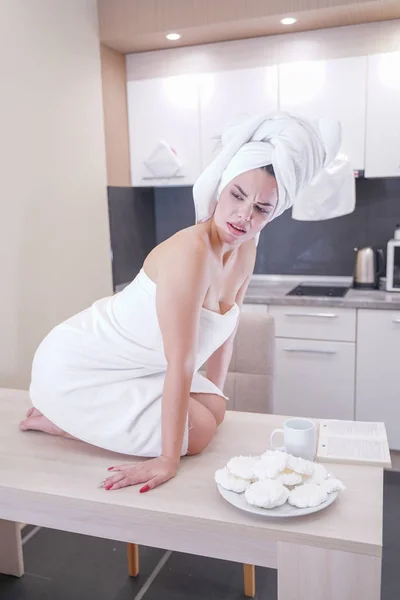 Jeune fille assise dans la cuisine après une douche enveloppée dans une serviette blanche et se reposant — Photo