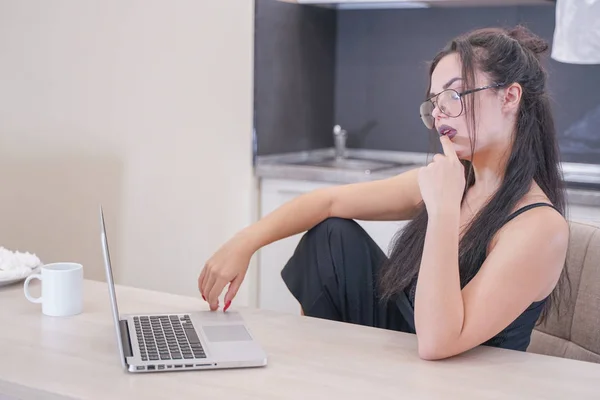 Menina bonito com óculos sentados à mesa com um laptop em casa sozinho — Fotografia de Stock