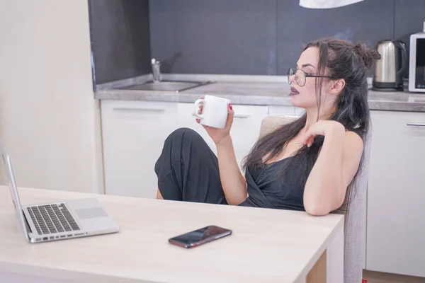 Menina bonito com óculos sentados à mesa com um laptop em casa sozinho — Fotografia de Stock