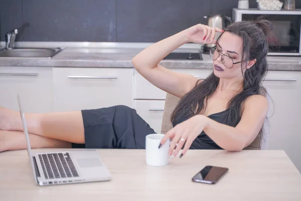 Menina bonito com óculos sentados à mesa com um laptop em casa sozinho — Fotografia de Stock