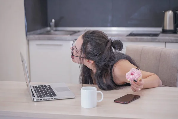 Søt jente med briller sittende ved bordet med en bærbar PC hjemme alene – stockfoto