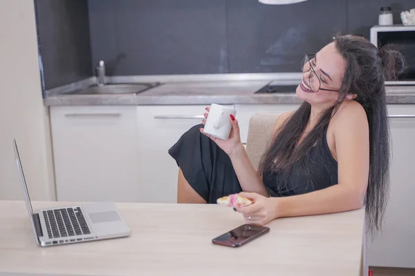 Милая девушка в очках сидит за столом с ноутбуком дома одна — стоковое фото