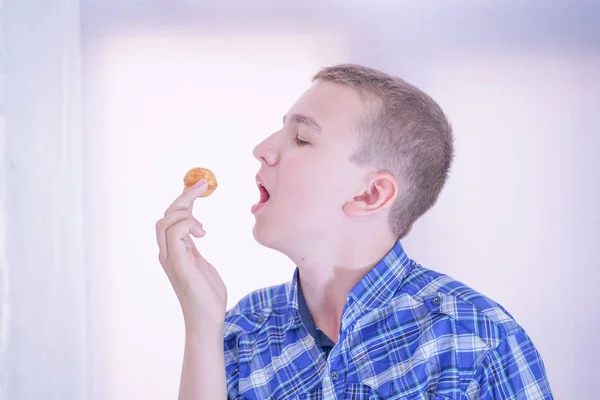 Bonito fome adolescente menino com fresco pequeno assar doces no branco quarto fundo sozinho — Fotografia de Stock