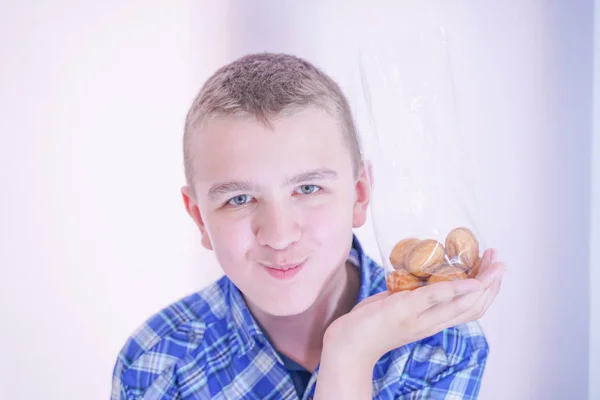 Schattige hongerige tiener jongen met verse kleine Bake snoepjes op witte kamer achtergrond alleen — Stockfoto