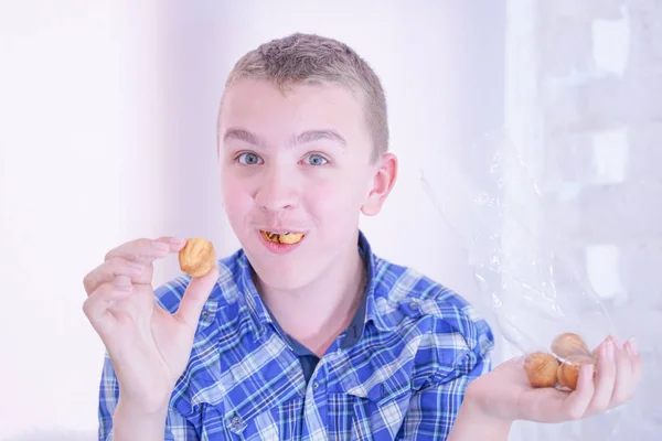 Schattige hongerige tiener jongen met verse kleine Bake snoepjes op witte kamer achtergrond alleen — Stockfoto