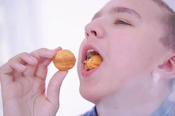 Schattige hongerige tiener jongen met verse kleine Bake snoepjes op witte kamer achtergrond alleen — Stockfoto