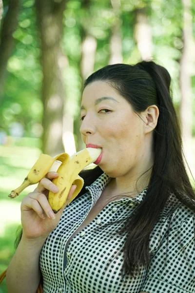 Pretty plus size asian girl eating banana in the city summer park alone — Stock Photo, Image