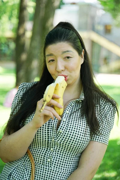 Девочка ест банан в городском летнем парке в одиночку — стоковое фото