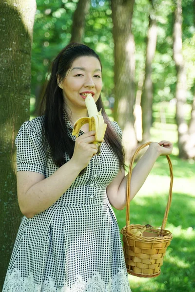 Pretty plus size asian girl eating banana in the city summer park alone — Stock Photo, Image