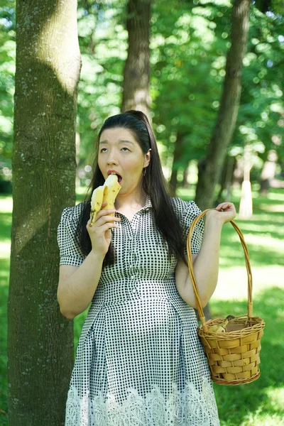 Pretty plus size asian girl eating banana in the city summer park alone — Stock Photo, Image