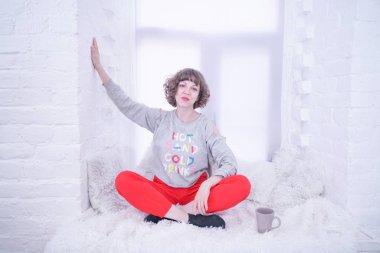 Beyaz pencere üzerinde oturan güzel yetişkin kadın.