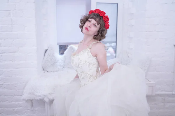 Ενηλίκων μοντέλο μόδας φορώντας κόκκινα τριαντάφυλλα στο κεφάλι και λευκό γάμο νύφη φόρεμα σε λευκό φόντο. — Φωτογραφία Αρχείου