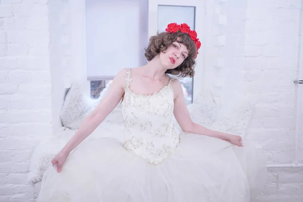 Modèle de mode adulte portant des roses rouges sur la tête et robe de mariée blanche sur fond blanc . — Photo