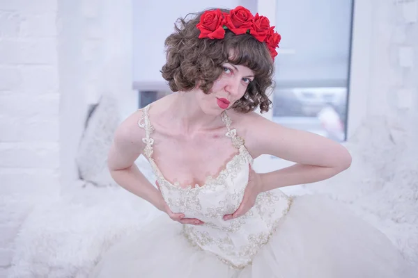 Modèle de mode adulte portant des roses rouges sur la tête et robe de mariée blanche sur fond blanc . — Photo