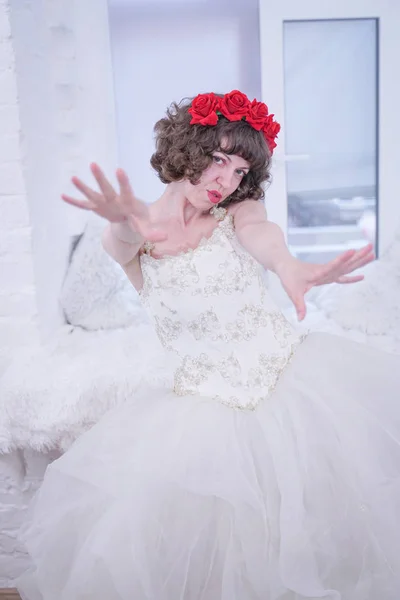 Modelo de moda adulta usando rosas vermelhas na cabeça e vestido de noiva de casamento branco no fundo branco . — Fotografia de Stock