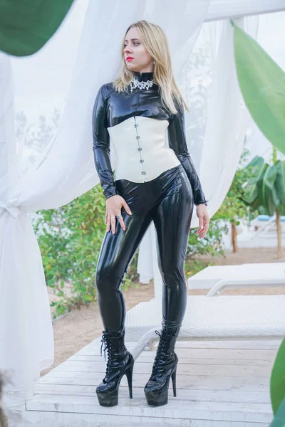 Стройная молодая блондинка из рабства в черном латексном костюме с белым корсетом — стоковое фото