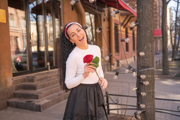 Joven hermosa chica bonita con el pelo largo con rosa roja en la ciudad — Foto de Stock