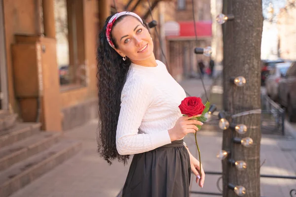 Joven hermosa chica bonita con el pelo largo con rosa roja en la ciudad —  Fotos de Stock