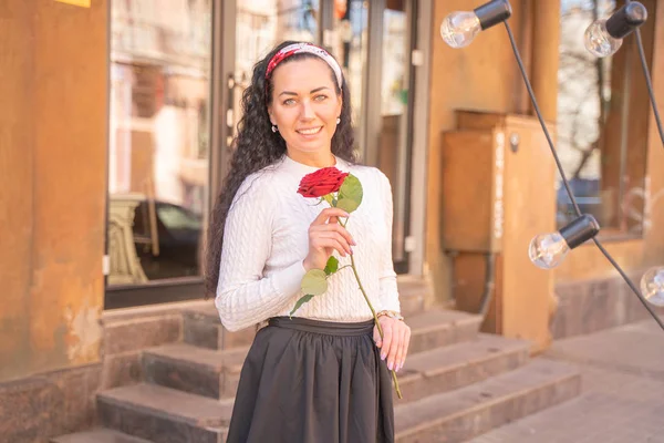 Joven hermosa chica bonita con el pelo largo con rosa roja en la ciudad — Foto de Stock