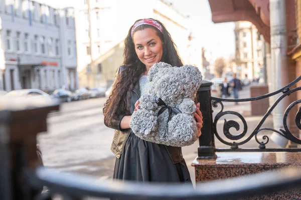 Bastante alegre chica adulta feliz con oso de peluche gris de rosas en la ciudad —  Fotos de Stock