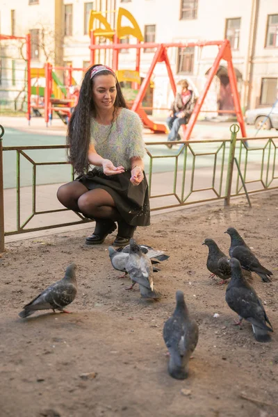 Mujer joven alimentando palomas en el parque de la ciudad — Foto de Stock
