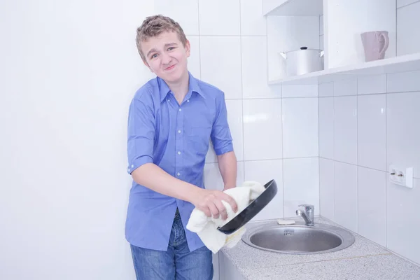 Um menino adolescente bonito lavar pratos na cozinha branca sozinho — Fotografia de Stock
