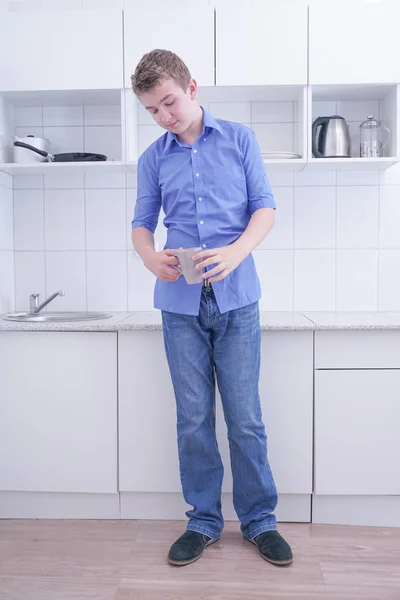 Young bored teenager very tired and stand with cup of coffee at his white kitchen — Stock Photo, Image