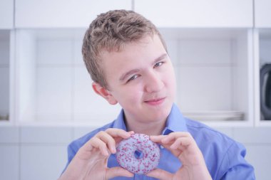 Küçük mutlu sevimli çocuk tek başına beyaz mutfak arka plan üzerinde donut yiyor