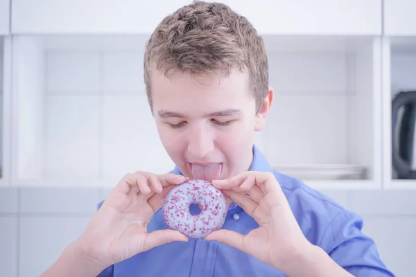Little happy cute boy is eating donut on white kitchen background alone — Stock Photo, Image