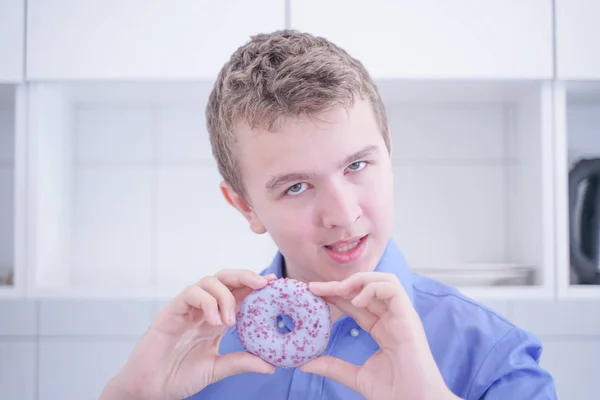 Little happy cute boy is eating donut on white kitchen background alone — Stock Photo, Image