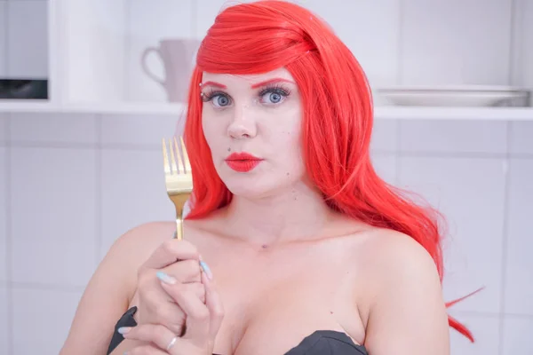 Beyaz mutfakta çatal tutan kırmızı saçlı siyah korse kız — Stok fotoğraf
