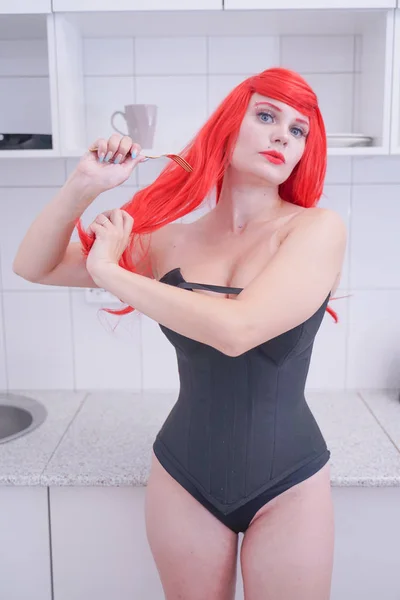 Fille en corset noir avec des cheveux rouges tenant fourchette dans la cuisine blanche — Photo
