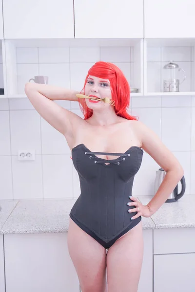 Fille en corset noir avec des cheveux rouges tenant fourchette dans la cuisine blanche — Photo