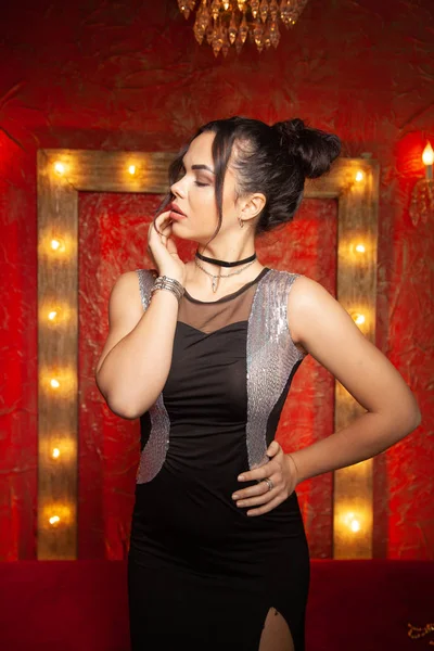 Cheerful young woman wearing party dress in red fashion room with light bulbs — Stock Photo, Image