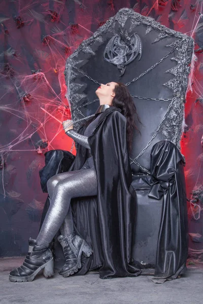Chica gótica futurista en catsuit brillante plateado en silla de trono negro —  Fotos de Stock