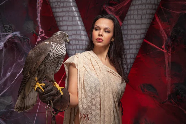 Beauty brunette girl and a hawk on dark gothic scary studio background — Stock Photo, Image