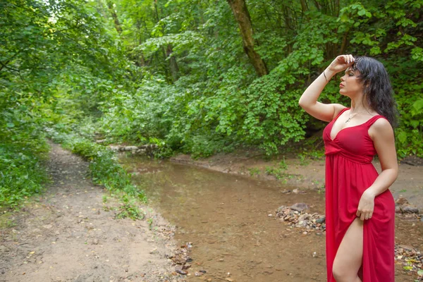 Gyönyörű lány egy elegáns piros ruháját jelentő a tündér erdőben. — Stock Fotó